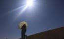 Una mujer se protege del sol con una sombrilla mientras camina por la calle