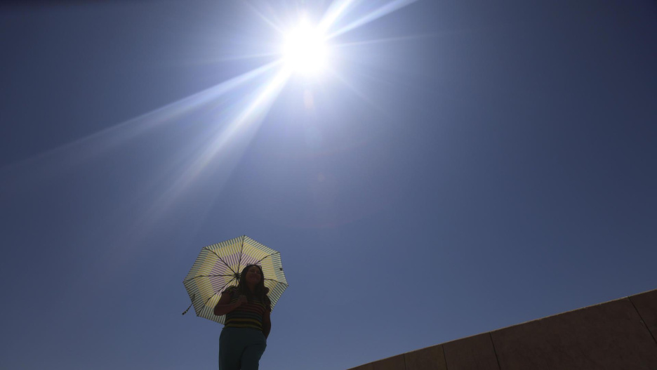 Una mujer se protege del sol con una sombrilla mientras camina por la calle