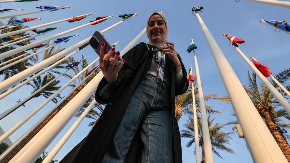 Dubai (United Arab Emirates), 11/12/2023.- A woman takes a selfie next to flags during the COP28 Conference in Dubai, United Arab Emirates, 11 December 2023. The 2023 United Nations Climate Change Conference (COP28), runs from 30 November to 12 December, and is expected to host one of the largest number of participants in the annual global climate conference as over 70,000 estimated attendees, including the member states of the UN Framework Convention on Climate Change (UNFCCC), business leaders, young people, climate scientists, Indigenous Peoples and other relevant stakeholders will attend. (Emiratos Árabes Unidos) EFE/EPA/ALI HAIDER