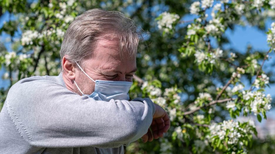 Un hombre con mascarilla estornuda debido a la alergia