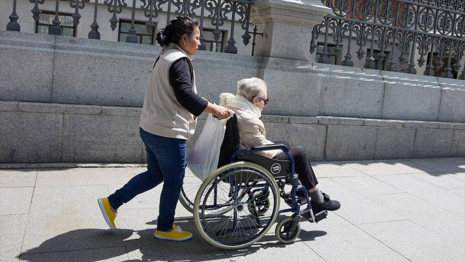 Una mujer mayor en silla de ruedas y su cuidadora pasean por el centro de la ciudad, a 4 de junio de 2023, en Madrid (España).