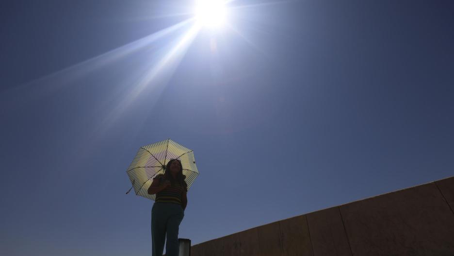 Una mujer se protege del sol con una sombrilla mientras camina por la calle