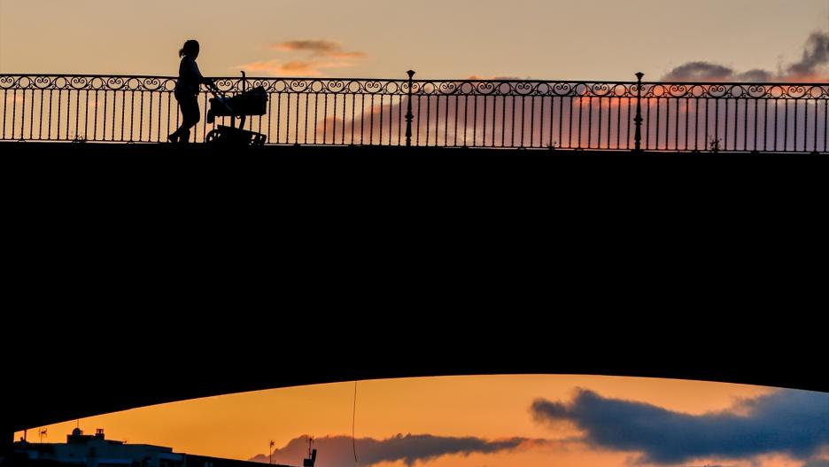 Una madre con un carrito de bebe paseando al atardecer.