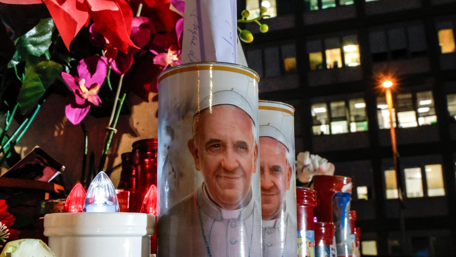 ROME (Italy), 21/02/2025.- Candles with the pictures of Pope Francis and flowers lay at the foot of a statue of Pope St. John Paul II outside Gemelli University Hospital, where Pope Francis is hospitalized for bronchitis treatment, in Rome, Italy, 21 February 2025. Pope Francis was hospitalized on 14 February due to a respiratory tract infection. (Papa, Italia, Roma) EFE/EPA/GIUSEPPE LAMI