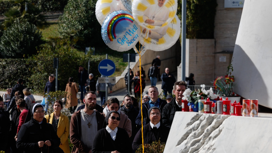 La gente reza bajo la estatua del difunto Papa Juan Pablo II en las afueras del Hospital Agostino Gemelli, donde el Papa Francisco está hospitalizado para continuar sus tratamientos para la neumonía bilateral, en Roma, Italia,