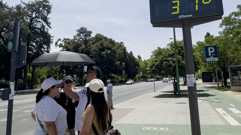 SEVILLA, 01/06/2025.- Varias personas conversa bajo un termómetro que marca 37 grados este domingo en Sevilla. EFE/David Arjona