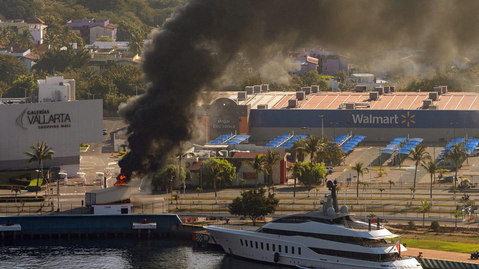 FOTODELDÍA MEX5107. PUERTO VALLARTA (MÉXICO), 22/02/2026.- Fotografía aérea donde se ve camión incendiándose tras reacciones violentas por el abatimiento de Nemesio Rubén Oseguera Cervantes, alias 'El Mencho', líder del Cártel Jalisco Nueva Generación (CJNG) este domingo, en Puerto Vallarta (México). El abatimiento de alias El Mencho desató una ola de violencia y bloqueos carreteros en México. EFE/ Gerardo Santillán